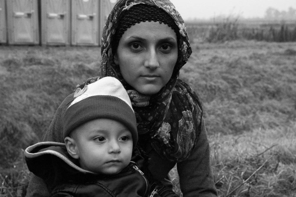 «Γυναίκα από Αφγανιστάν με το παιδί της, στο Ζακανύ (Ουγγαρία), σύνορα με Μπότοβο (Κροατία), πριν επιβιβαστεί στο τελευταίο έκτακτο τρένο της ημέρας προς τον τελευταίο σταθμό  πριν την Αυστρία, το Χεγκγιέσαλομ (Ουγγαρία). 13-10-2015»
